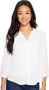 A female model wearing a white-colored NYDJ Women's Petite Size 3/4 Sleeve Pintuck Blouse. One of the best tunic tops for women to wear with leggings